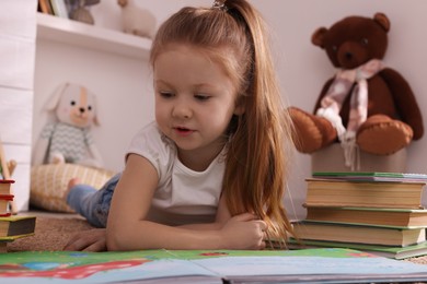 Cute little girl reading book on floor at home