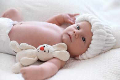 Photo of Cute newborn baby with toy in white knitted hat on plaid