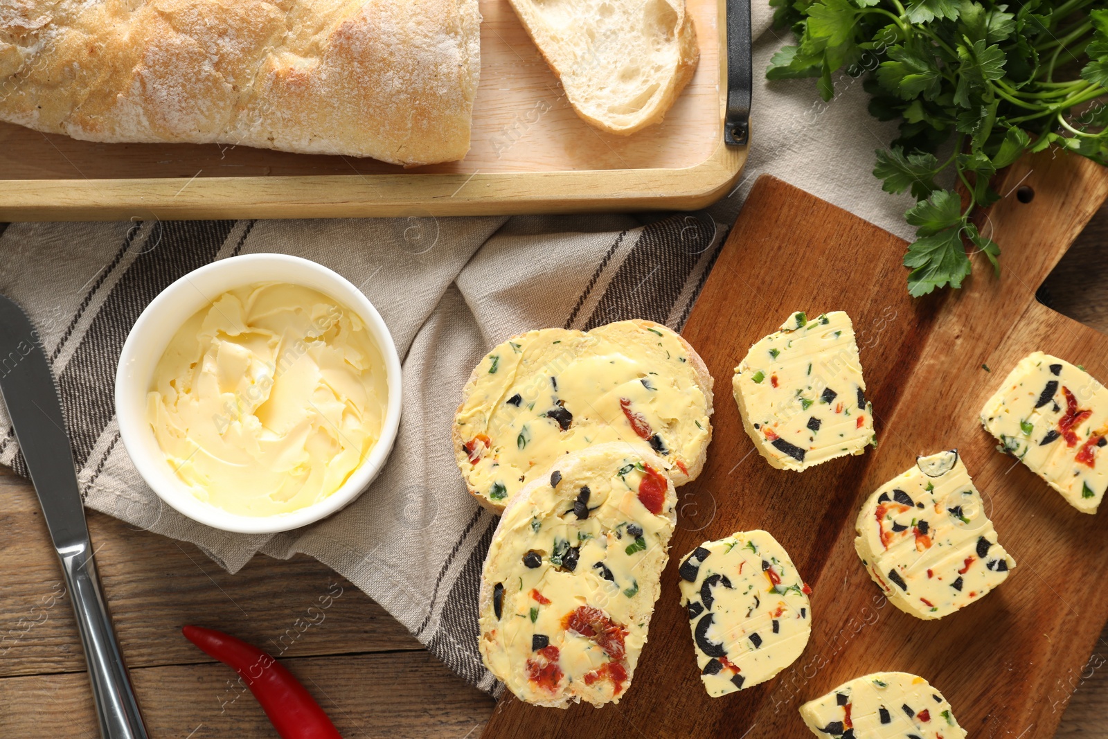 Photo of Tasty butter with olives, chili pepper, parsley and bread on wooden table, top view