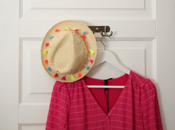 Photo of Clothes hooks with blouse and straw hat on white door