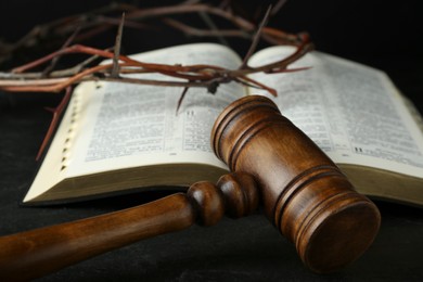 Photo of Judge gavel, bible and crown of thorns on black table, closeup