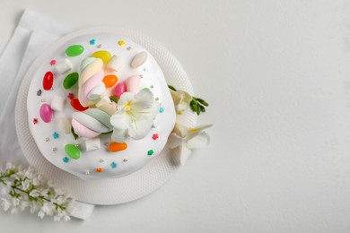 Photo of Traditional Easter cake with sprinkles, jelly beans and marshmallows on white table, flat lay. Space for text