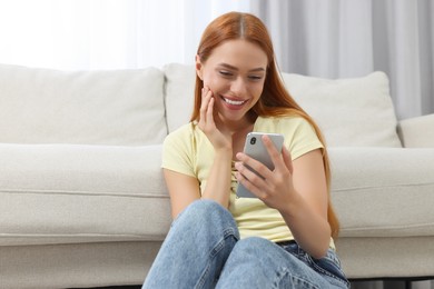 Photo of Happy young woman having video chat via smartphone at home