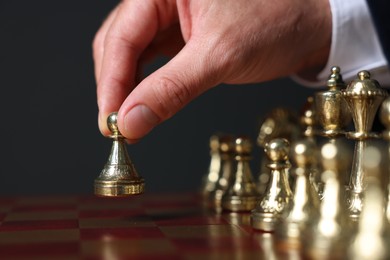 Man with game piece playing chess at board against dark background, closeup