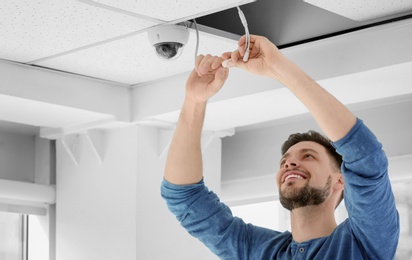 Photo of Technician installing CCTV camera on ceiling indoors