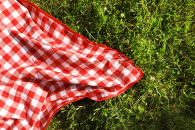 Checkered picnic tablecloth on fresh green grass, top view. Space for text