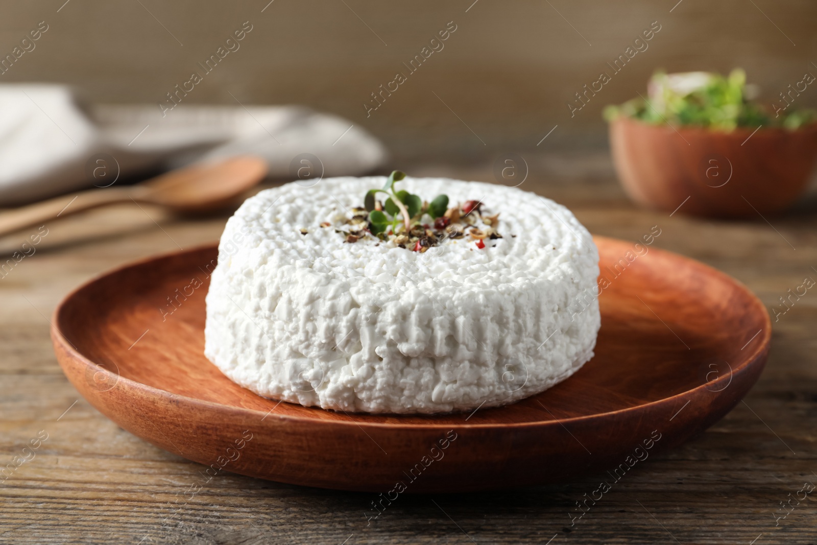 Photo of Wooden plate of fresh cottage cheese with spice and microgreens on table, closeup