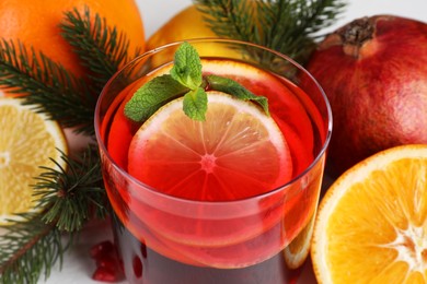 Photo of Christmas Sangria drink in glass, fir branches and fruits on white background, closeup