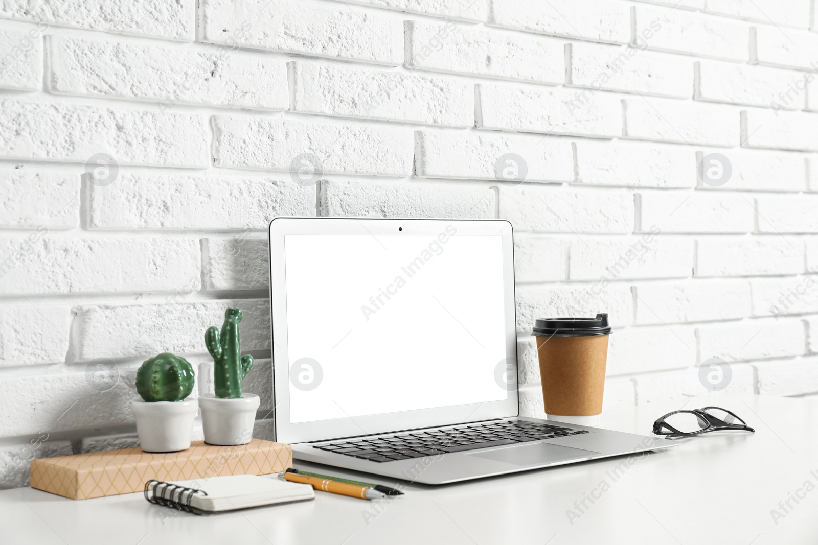 Photo of Modern workplace with laptop on table near brick wall. Space for design