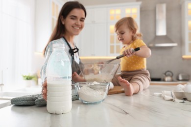 Photo of Mother and her little daughter cooking dough together in kitchen, focus on bottle of milk. Space for text