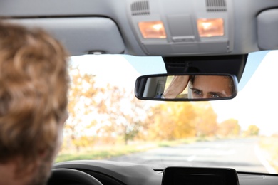 Photo of Young handsome man looking into interior mirror in car