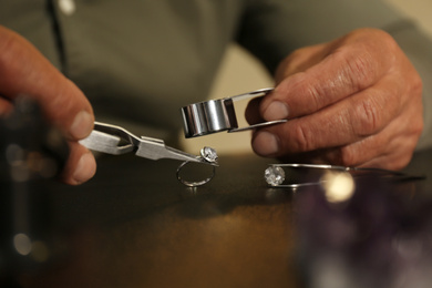 Professional jeweler working with beautiful ring at table, closeup
