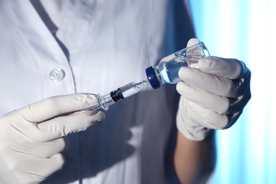 Doctor filling syringe with vaccine from vial on blurred background, closeup