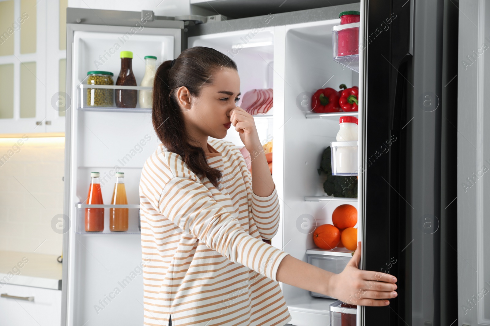 Photo of Young woman holding nose cause of bad smell in refrigerator in kitchen