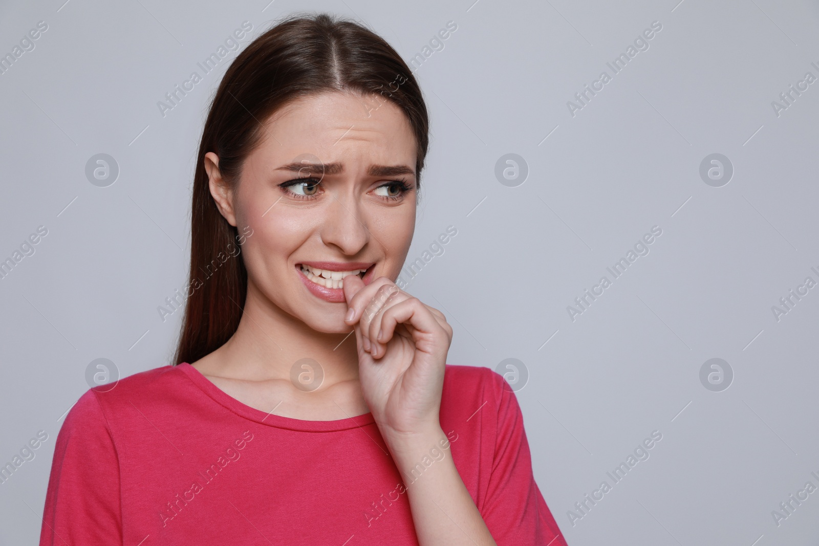 Photo of Young woman biting her nails on light grey background. Space for text