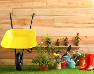 Wheelbarrow with gardening tools and flowers near wooden wall