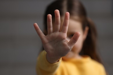 Photo of Child abuse. Little girl doing stop gesture on gray background, selective focus