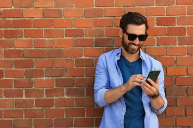 Happy man with smartphone near red brick wall. Space for text