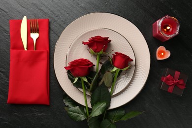 Photo of Place setting with candles, gift box and roses on grey textured table, flat lay. Romantic dinner