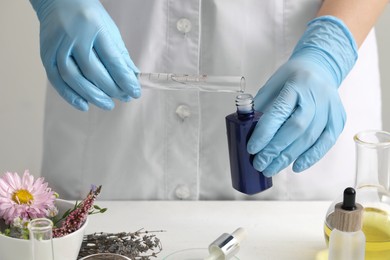 Photo of Scientist developing cosmetic oil at white table, closeup