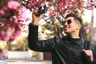 Photo of Happy male tourist taking photo of blossoming sakura outdoors on spring day