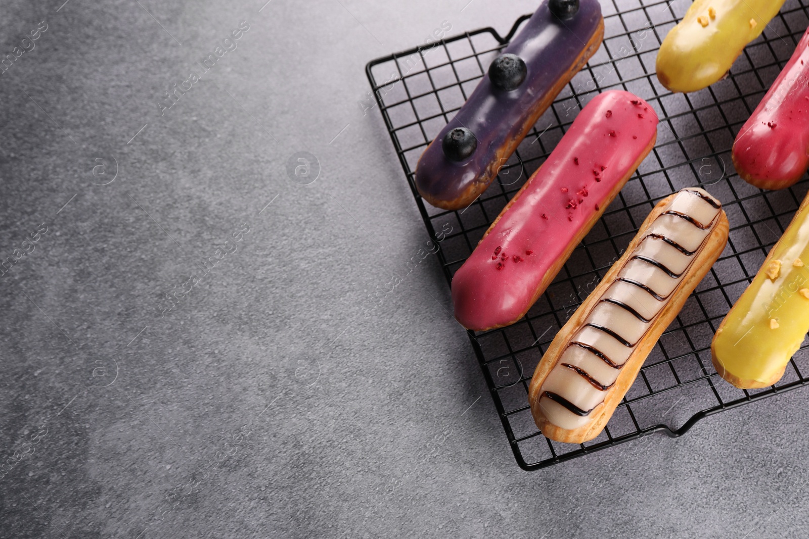 Photo of Cooling rack with different tasty glazed eclairs on grey table, above view. Space for text