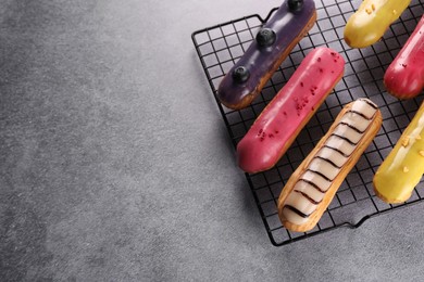 Cooling rack with different tasty glazed eclairs on grey table, above view. Space for text