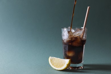 Photo of Pouring coffee into glass with ice cubes on green background, closeup. Space for text