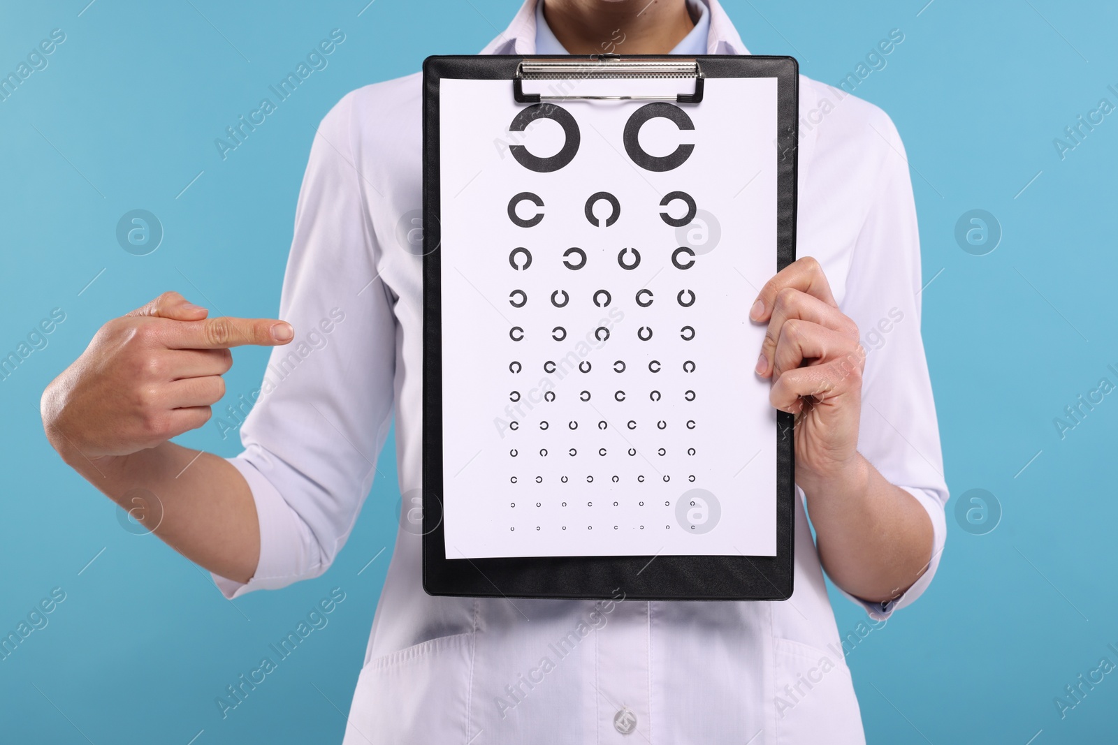 Photo of Ophthalmologist pointing at vision test chart on light blue background, closeup