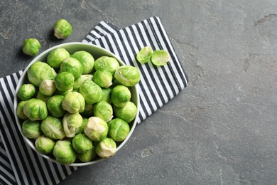 Photo of Bowl of fresh Brussels sprouts and napkin on grey background, top view with space for text
