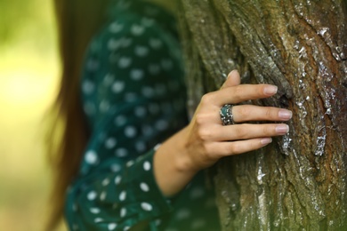 Photo of Young woman wearing beautiful silver ring with apatite gemstone near tree outdoors, closeup