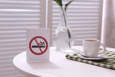 Photo of No Smoking sign and cup of coffee on white table indoors