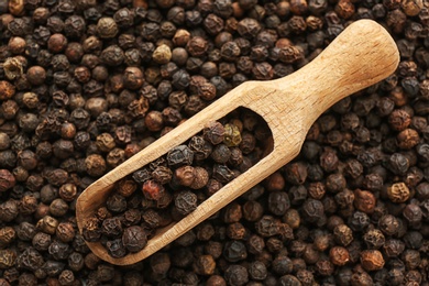 Photo of Scoop with black pepper on heap of grains, top view