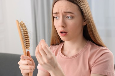 Emotional woman untangling her lost hair from brush at home. Alopecia problem