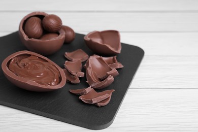Broken and whole chocolate eggs with paste on white wooden table, closeup. Space for text