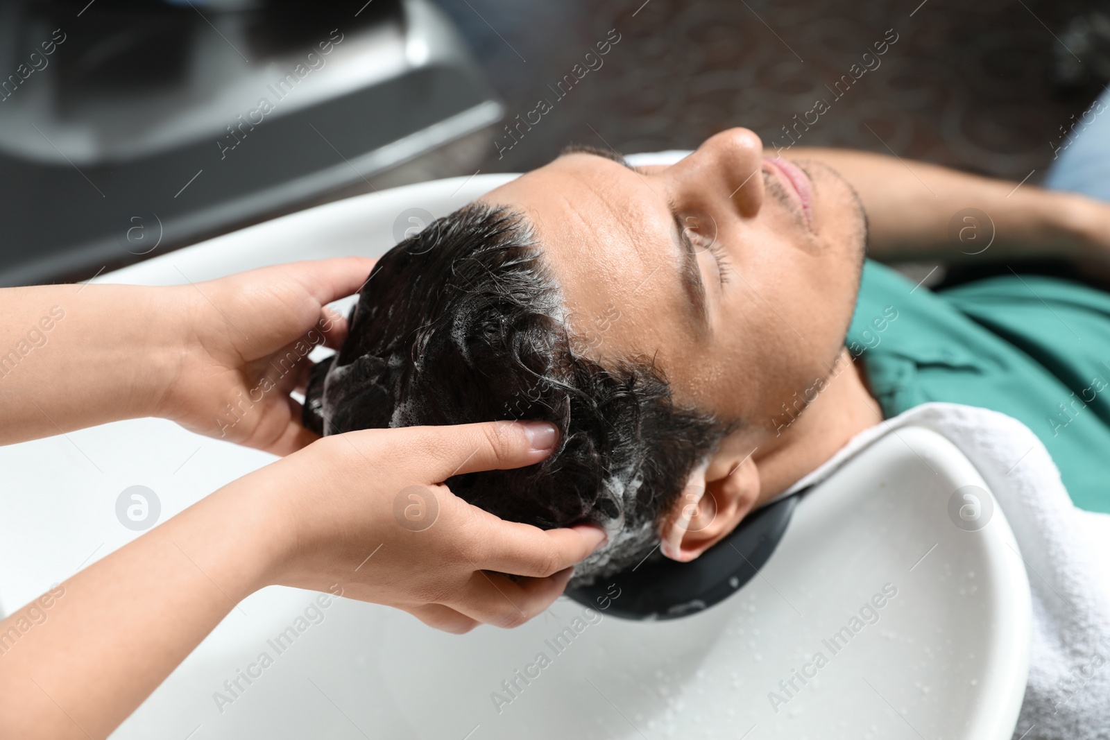 Photo of Stylist washing client's hair at sink in beauty salon