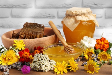 Delicious honey, combs and different flowers on wooden table near white brick wall