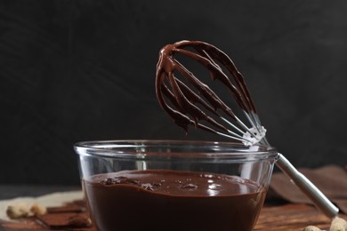 Bowl of chocolate cream and whisk on table against dark background, closeup