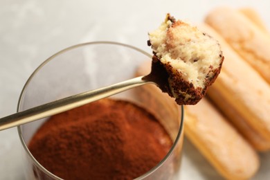 Tasty tiramisu in glass, spoon and biscuits on light grey table, closeup