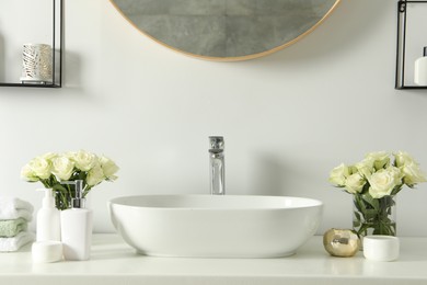 Photo of White sink between beautiful roses and toiletries in bathroom