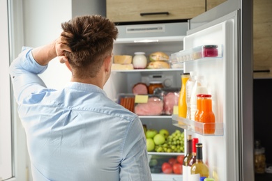 Man looking into refrigerator full of products in kitchen