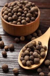 Dry allspice berries (Jamaica pepper) in bowl and spoon on wooden table, closeup