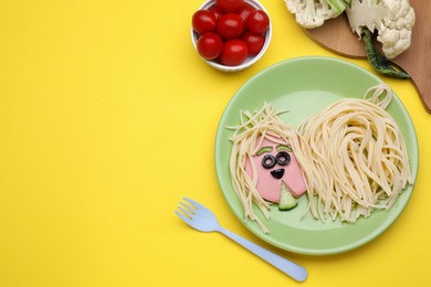 Photo of Creative serving for kids. Plate with cute dog made of tasty pasta, sausage and cucumber on yellow table, flat lay. Space for text