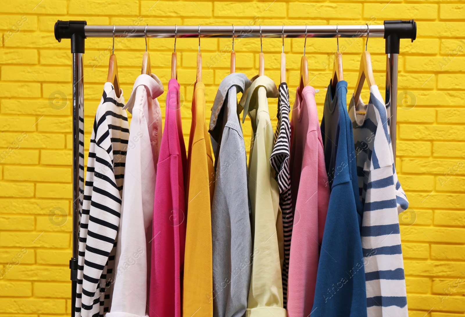 Photo of Rack with different stylish clothes near yellow brick wall