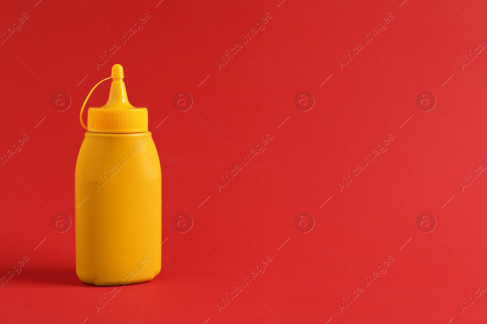 Photo of Spicy mustard in plastic bottle on red background, space for text