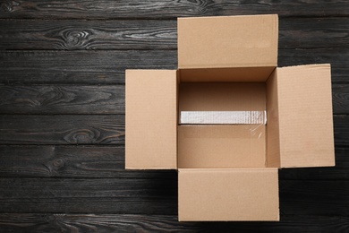 Photo of Open cardboard box on black wooden background, top view. Space for text