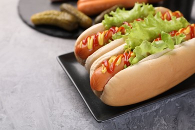 Photo of Tasty hot dogs with lettuce, ketchup and mustard on grey textured table, closeup. Space for text