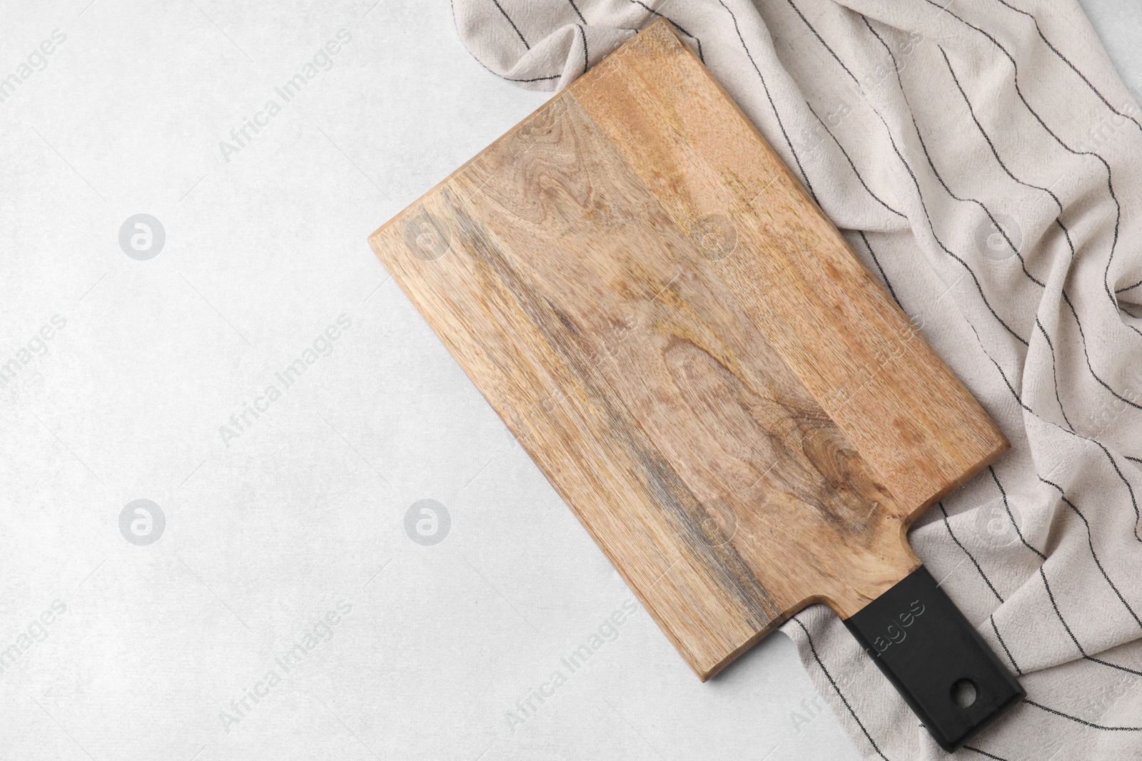 Photo of One wooden cutting board and tablecloth on light grey table, top view with space for text. Cooking utensil