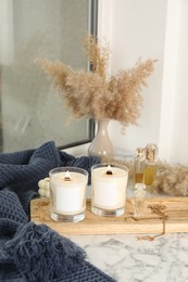 Burning soy candles, perfumes, blanket and stylish accessories on white window sill indoors