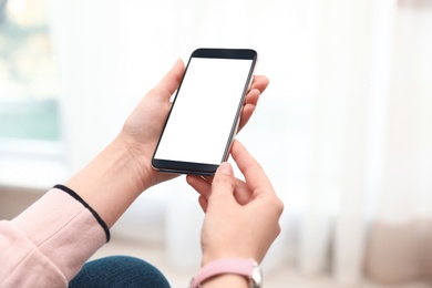 Woman holding smartphone with blank screen indoors, closeup of hands. Space for text